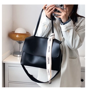 Detail of black faux leather shoulder bag with a white woven strap featuring text