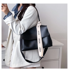 Minimalist black leather shoulder bag with stylish lettered strap shown in use
