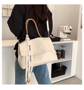 Detail view of cream shoulder bag with brown handle and elegant logo silk ribbon accessory