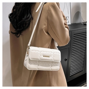 Detail einer weißen Stepptasche mit goldener Hardware, getragen auf einem Blazer