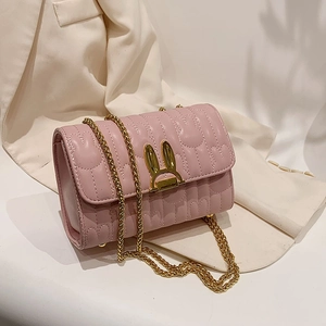 Pink quilted crossbody bag with golden rabbit ear lock and chain strap on blazer background