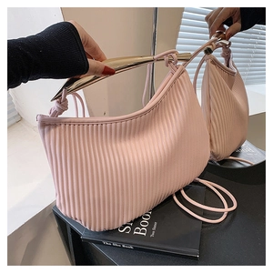 Macro shot of light pink pleated handbag featuring elegant curved gold metal handle and strap