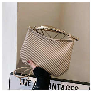 Detail of minimalist pleated beige square bag featuring a gold metallic curved handle
