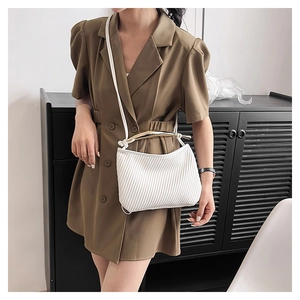 Detail of white pleated handbag featuring a golden curved handle and refined textures