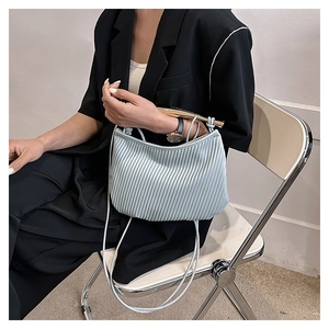 Detail of light blue pleated handbag with golden curved handle and slim strap