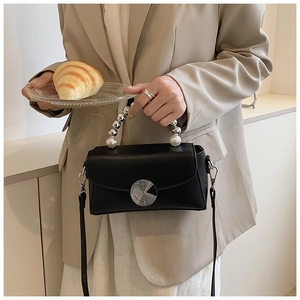 Detail of black mini crossbody bag featuring pearl and silver ball handle and metal clasp