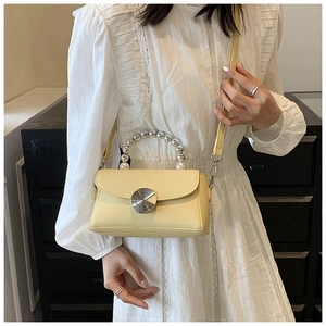 Detail of cream crossbody bag with pearl handle and metal lock worn by a model