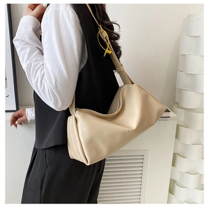 Beige minimalist dumpling shoulder bag with wide strap worn by model in a modern setting