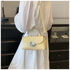 Detail of elegant cream handbag with pearl handle and silver lock shown on a white dress