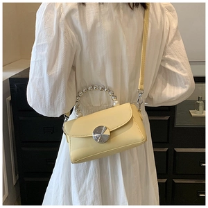 Detail of a creamy yellow crossbody bag featuring a luxury pearl and metal bead handle