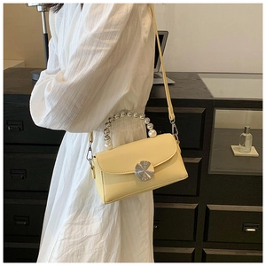 Detail of light yellow crossbody bag with pearl handle and silver sunburst lock buckle