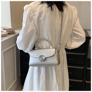 Close-up of a silver crossbody bag featuring a pearl handle and metal twist lock detail