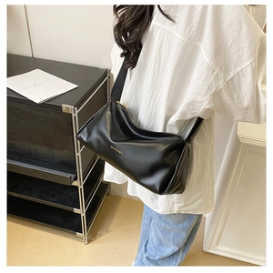 Close-up of black glossy leather underarm bag with gold logo on shoulder of a model