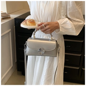 Detail of silver mini crossbody bag featuring pearl handle and stylish metallic rotary knob