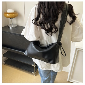 Detail of a black PU leather underarm bag with a wide shoulder strap shown on a model