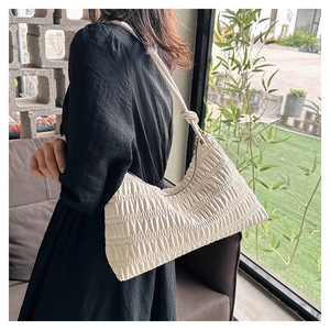 Close-up of a white pleated underarm bag with refined knot detail and metal zipper