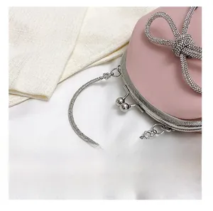 Detail view of a light pink shell bag featuring a sparkling rhinestone bow and metal handle