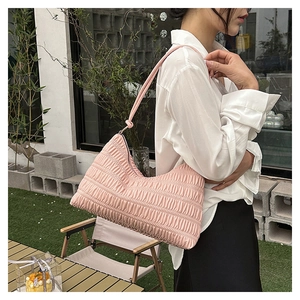 Detail of pink pleated shoulder bag with vertical quilting texture in outdoor setting