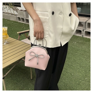 Outdoor view of a pink shell handbag with a large rhinestone bow and silver handle