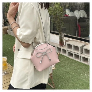 Pink seashell-shaped crossbody bag with rhinestone bow detail on white suit