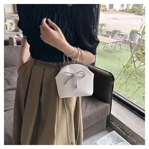 Detail view of white shell bag with crystal bow, pearl handle, and chain strap