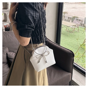 Close-up of white shell bag featuring a sparkling rhinestone bow and silver chain strap