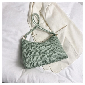 Close-up of light green pleated shoulder bag with gold hardware on white blazer