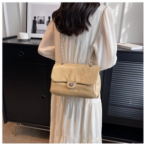 Détail d'un sac bandoulière matelassé beige avec chaîne porté par un mannequin pour la taille