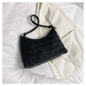 Detail of black smocked croissant bag with gold hardware on white fabric