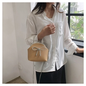 Detail view of milk tea leather handbag featuring a rhinestone bow and metal clasp