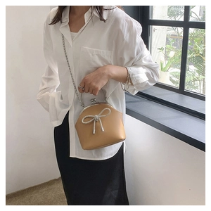 Detailed view of camel shell bag with rhinestone bow and metal clasp on female model