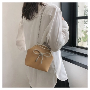 Khaki crossbody shell bag with rhinestone bow detail and silver chain strap on model