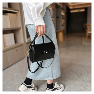 Side view of a black leather crossbody bag with top handle and metal buckle closure