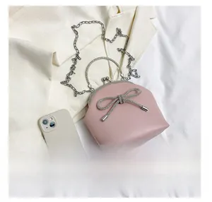 Detailed view of mini pink bow shell bag with metal handle beside phone for scale