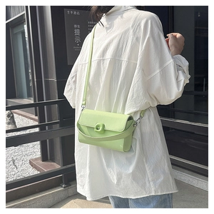 Detail of mint green crossbody bag worn over white shirt showing the square buckle