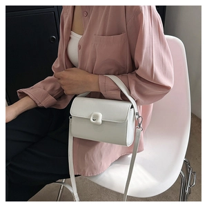 Detail view of a white minimalist leather crossbody bag worn by a model in a casual outfit