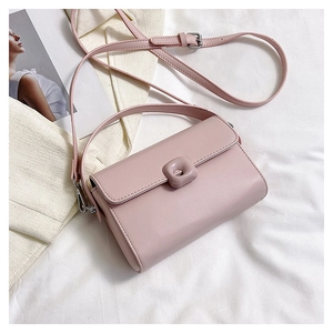 Top view of a stylish pink leather crossbody bag on white fabric with fashion accessories