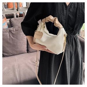 Détail du sac à main plissé blanc avec anse nuage beige et chaîne dorée sur robe noire