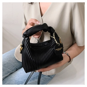 Détail d'un sac à main plissé noir avec poignée nouée et chaîne dorée porté par un mannequin