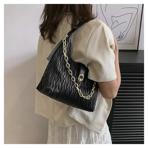 Dettaglio borsa a spalla nera a pieghe con catena dorata spessa su blazer beige
