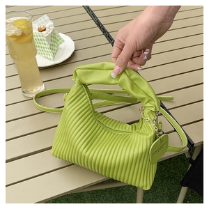 Gros plan du sac à main plissé vert herbe avec poignée texturée et étiquette mode sur table