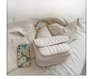 Close-up of cream quilted chain bag next to smartphone for size comparison
