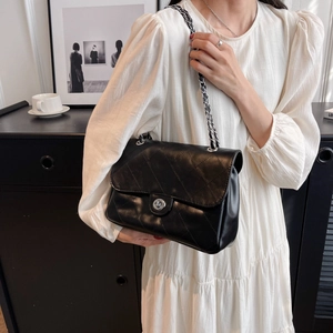 Sac bandoulière en cuir matelassé noir avec chaîne argentée sur robe blanche