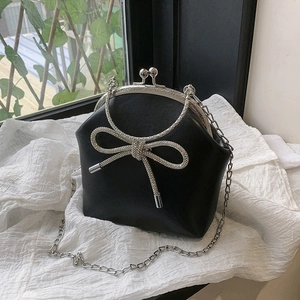 Elegant black shell bag with rhinestone bow and silver chain strap on white fabric