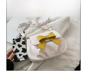 Dettaglio della borsa a tracolla bianco sporco con fiocco giallo e tracolla intrecciata