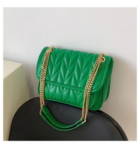 Detail of green quilted crossbody bag with V-shaped stitching and gold chain strap