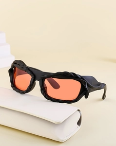 Detail of Y2K sunglasses with black textured frame and orange lenses on a white case