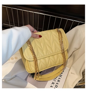 Detail of bright yellow quilted crossbody bag featuring elegant gold chain strap