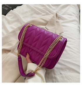 Detail of bright purple quilted leather bag featuring a gold chain strap held by a hand