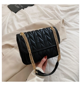 Detail of black wavy quilted chain bag with gold hardware on neutral background